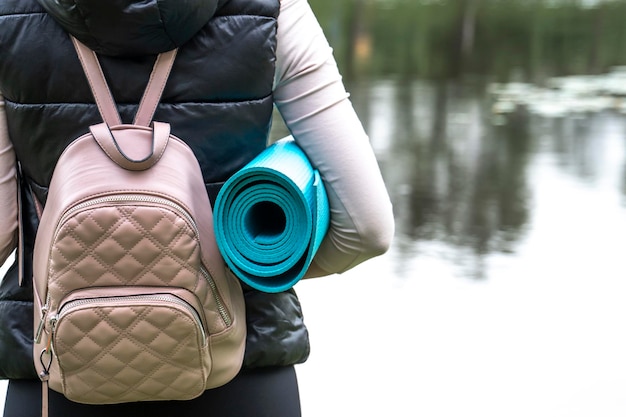 Young woman with backpack and yoga mat on lake mental health wellness reconnecting with nature