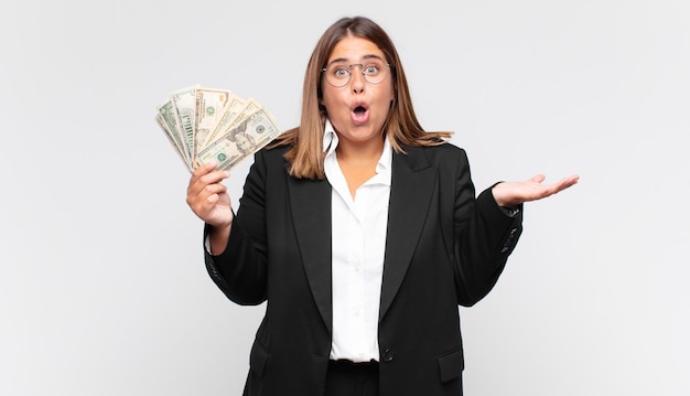 Young woman with banknotes open-mouthed and amazed, shocked and astonished with an unbelievable surprise