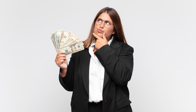 Young woman with banknotes thinking, feeling doubtful and confused, with different options, wondering which decision to make