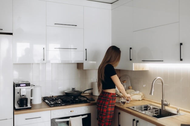 young woman with beautiful body standing next to a modern kitchen while cooking back view