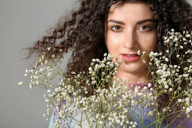 Young woman with beautiful curly hair and flowers on grey background