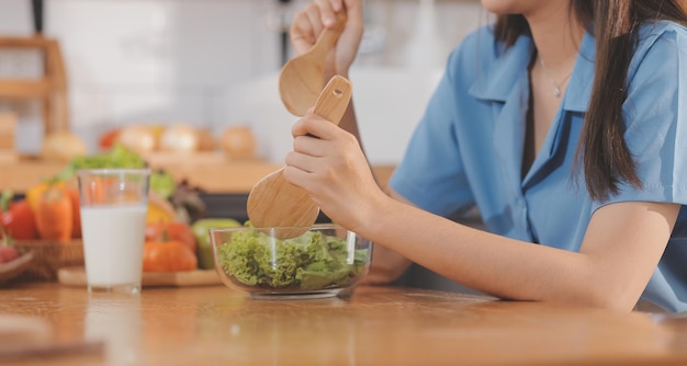 A young woman with a beautiful face in a blue shirt with long hair eating fruit sitting inside the kitchen at home with a laptop and notebook for relaxation Concept Vacation