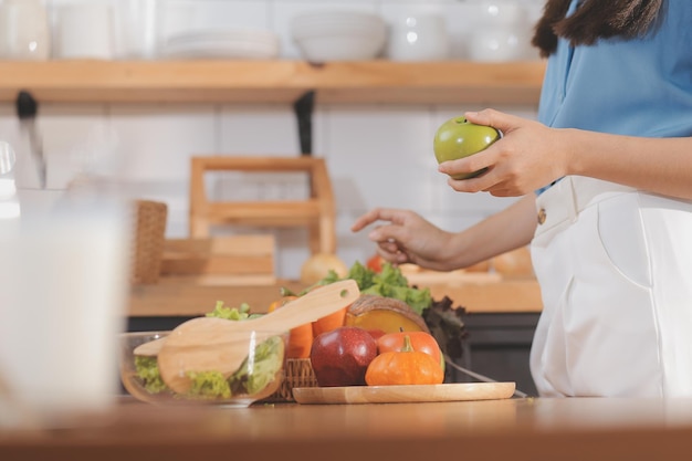 Молодая женщина с красивым лицом в голубой рубашке с длинными волосами ест фрукты сидит на кухне дома с ноутбуком и ноутбоком для отдыха Концепция отдыха