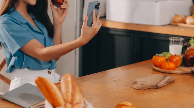 a young woman with a beautiful face in a blue shirt with long hair eating fruit sitting inside the kitchen at home with a laptop and notebook for relaxation concept vacation