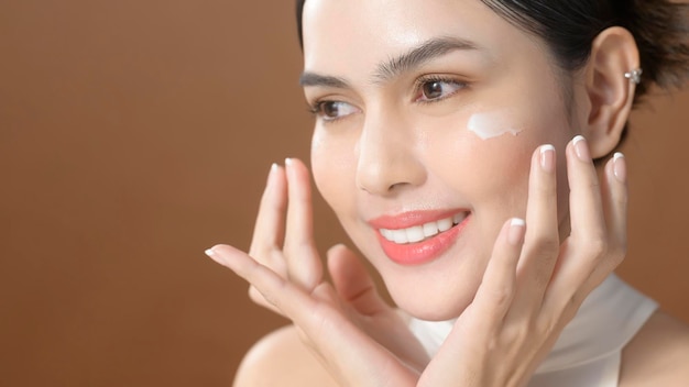 A young woman with beautiful face is holding cream using cream of her face beauty skin care concept