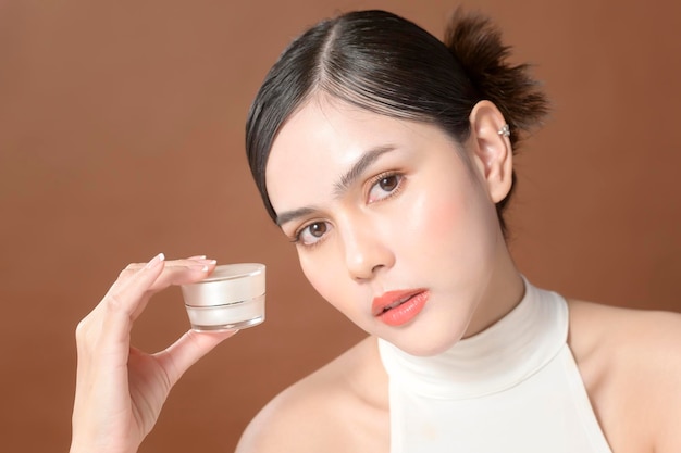 A young woman with beautiful face is holding cream using cream of her face beauty skin care concept