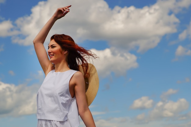 Young woman with beautiful red hair, blue cloudy sky on background