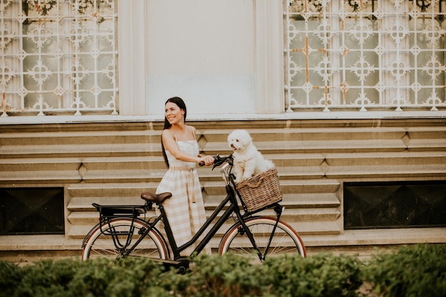 A young woman with a bichon dog in a bicycle basket takes a leisurely ride