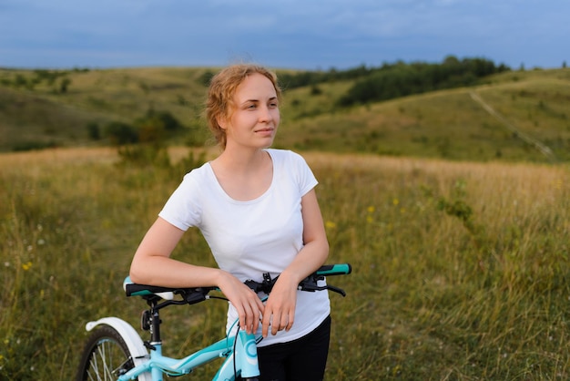 心地よい夕日を楽しむ野原で自転車を持つ若い女性