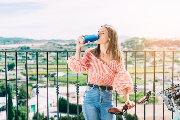 Foto giovane donna con una bicicletta che riposa e beve da una bottiglia