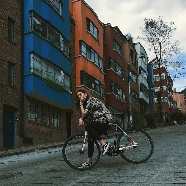 young woman with bicycle standing on street against buildings in city