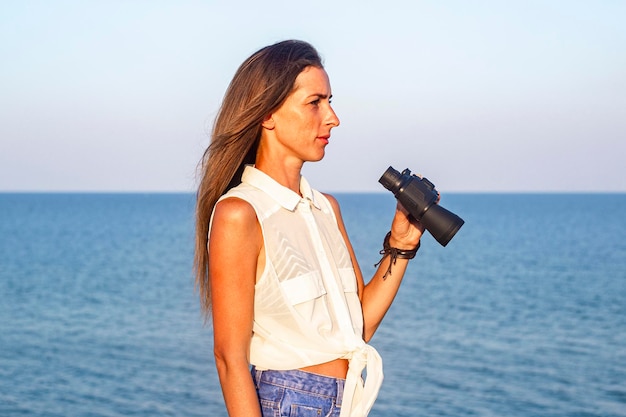 Young woman with binoculars on the cliff against the background of the sea.