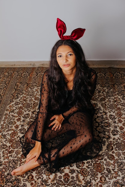 Giovane donna con abito nero e fiocco rosso tra i capelli. seduto su un vecchio tappeto. fotografia di moda.