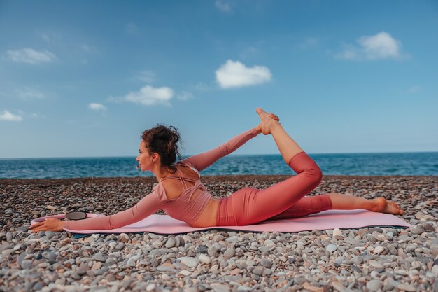 Giovane donna con i capelli neri istruttore di fitness in leggings e top facendo stretching e pilates su