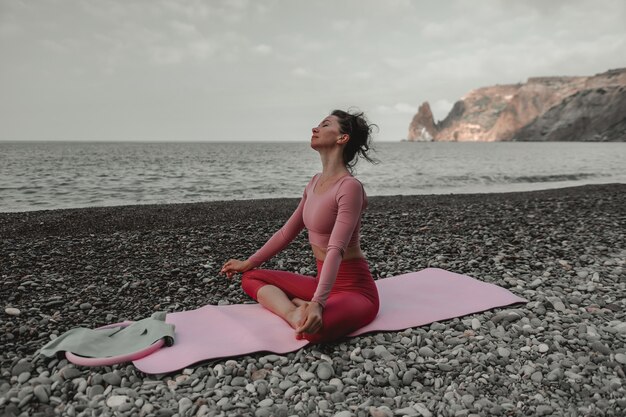 Young woman with black hair fitness instructor in leggings and tops doing stretching and pilates on