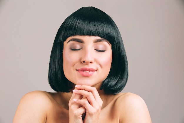 Young woman with black hair posing. Dreamy nice model keep eyes closed and hands together. Smile. Calm and peaceful.