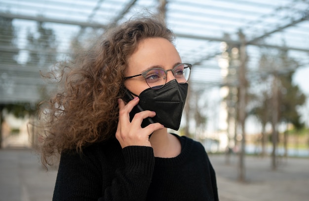 通りで電話で話している黒いマスクを持つ若い女性