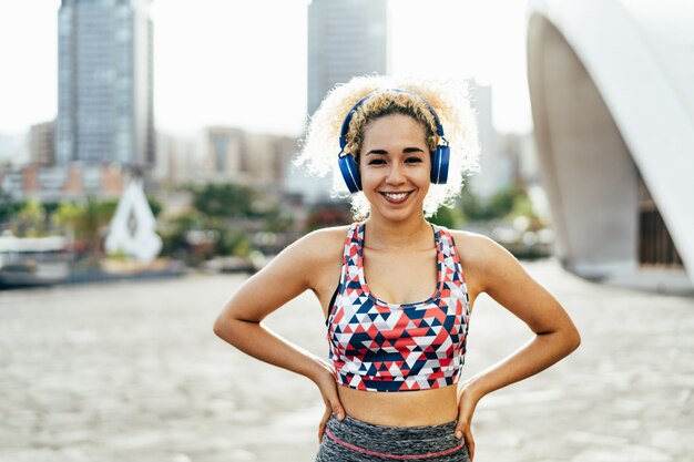 Молодая женщина со светлыми вьющимися волосами делает спорт на открытом воздухе во время прослушивания музыки плейлист