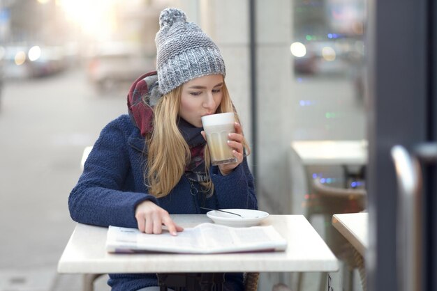 写真 歩道のカフェでコーヒーを飲んでいる金 ⁇ の若い女性