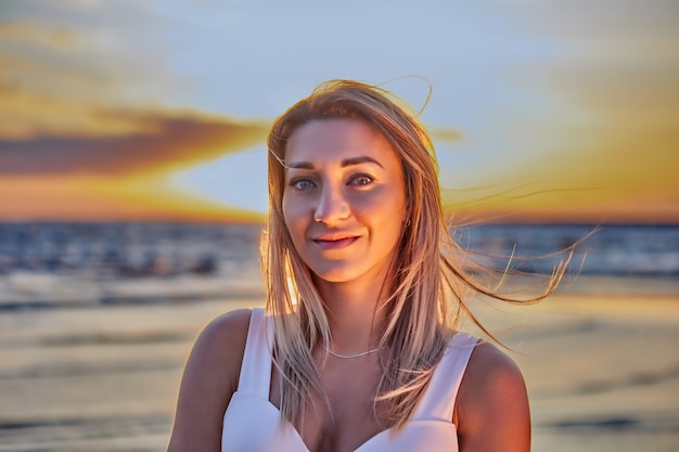 Young woman with blond hair stands on coast during sunset