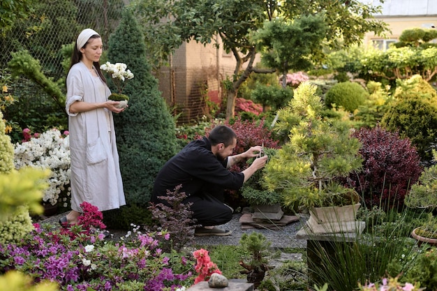 盆栽と男性の若い女性は、盆栽の庭で盆栽の木の枝を飾るためにハサミを使用しています