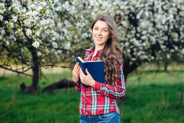 Young woman in with book in a blooming garden