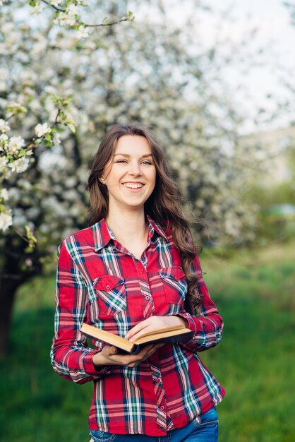 Young woman in with book in a blooming garden