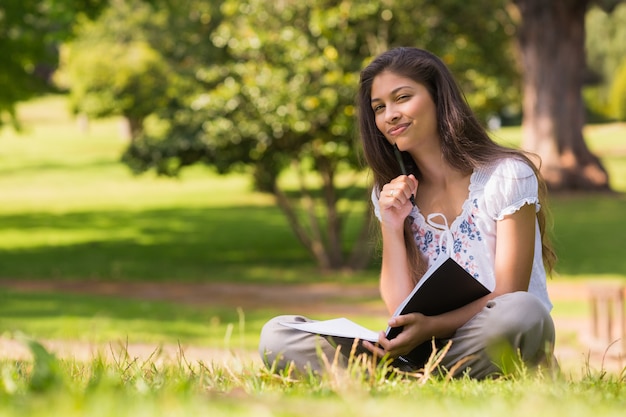 Young woman with book and pen sitting in park