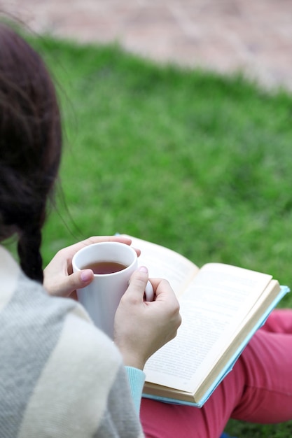 Young woman with book sitting on green grass outdoors