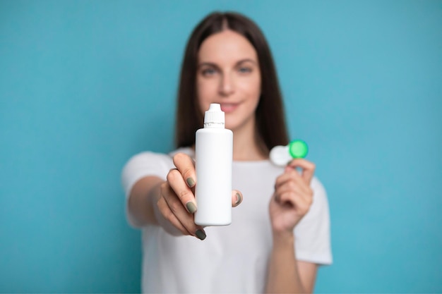 Young woman with bottle of solution and contact lenses on color background