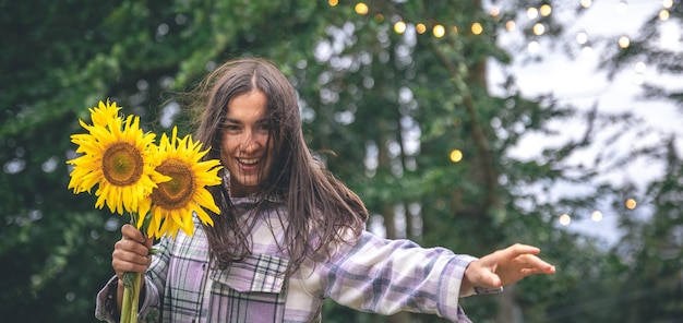 자연의 흐릿한 배경에 해바라기 꽃다발을 든 젊은 여성