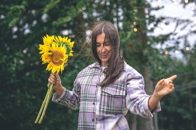 自然の中でぼやけた背景にひまわりの花束を持つ若い女性