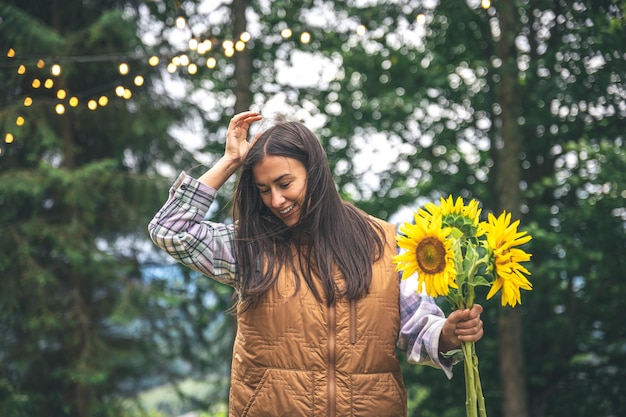 自然の中でぼやけた背景にひまわりの花束を持つ若い女性