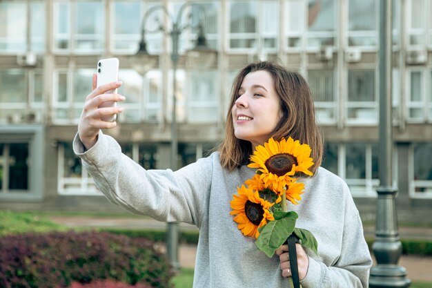 街でヒマワリの花束を持った若い女性がセルフィーを撮る