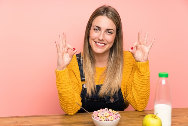 Young woman with bowl of cereals showing an ok sign with fingers