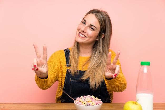 Young woman with bowl of cereals smiling and showing victory sign