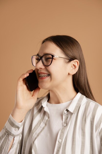 Photo young woman with braces call and talk on smartphone on beige background