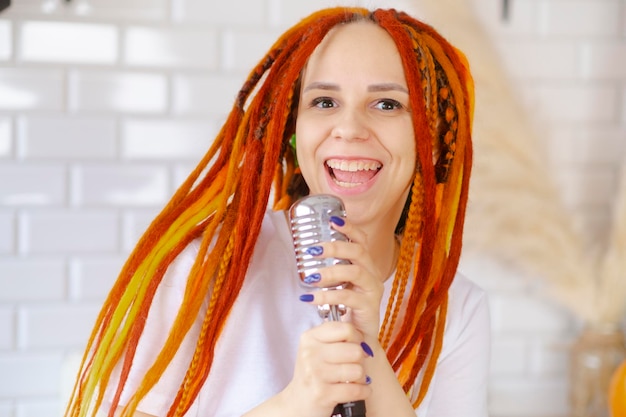 Young woman with bright hairstyle with retro microphone in kitchen Portrait of female singer with dreadlocks singing into microphone at home
