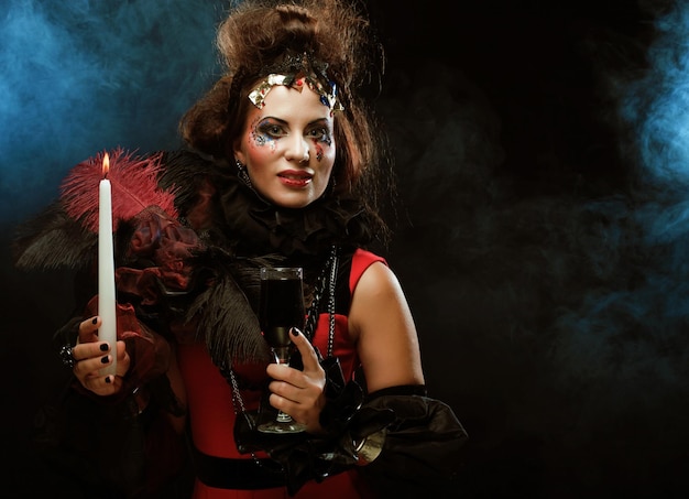 Молодая женщина с ярким макияжем в карнавальном костюме держит свечу на Хэллоуин