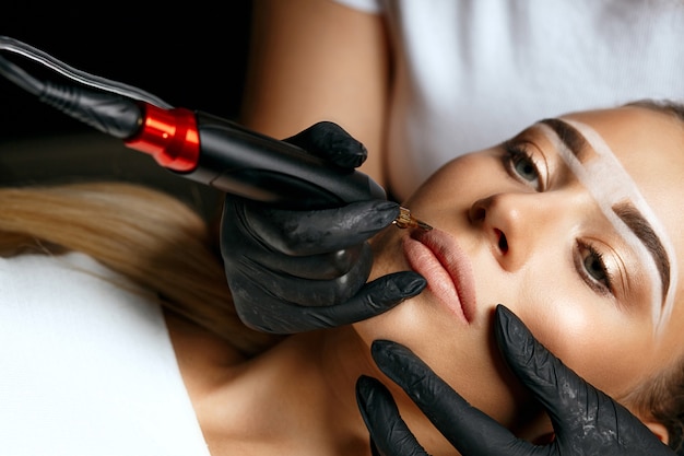 Young woman with brow paste on her brows having permanent makeup on lips in beauty salon