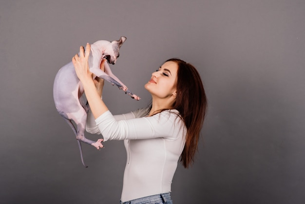 Young woman with canadian sphynx cat in a studio, grey background