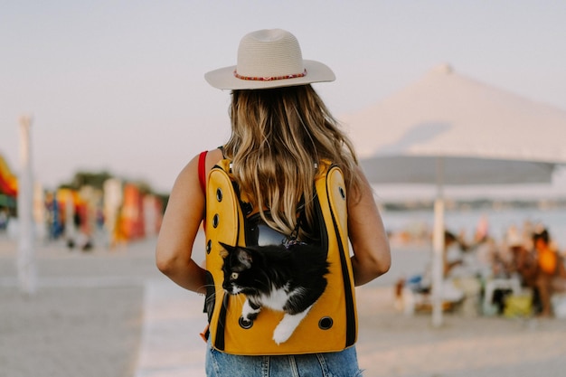 young woman with a cat in a backpack on the seashore. Travel concept with a pet. Cat in the backpack with porthole.