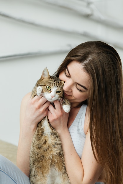 ベッドの上に座っている猫を持つ若い女性。明るい寝室の女の子。