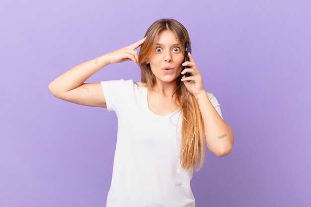 Young woman with a cell phone looking happy, astonished and surprised