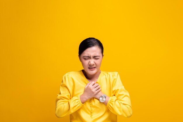 Young woman with chest pain against yellow background