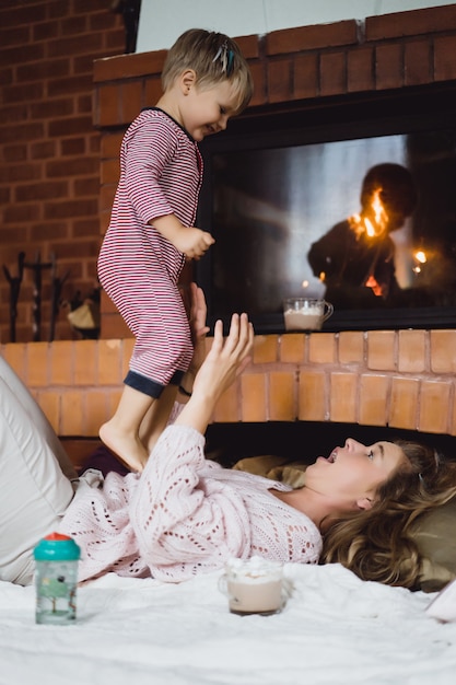 Foto giovane donna con un bambino. mamma e figlio stanno scherzando, divertendosi vicino al camino.