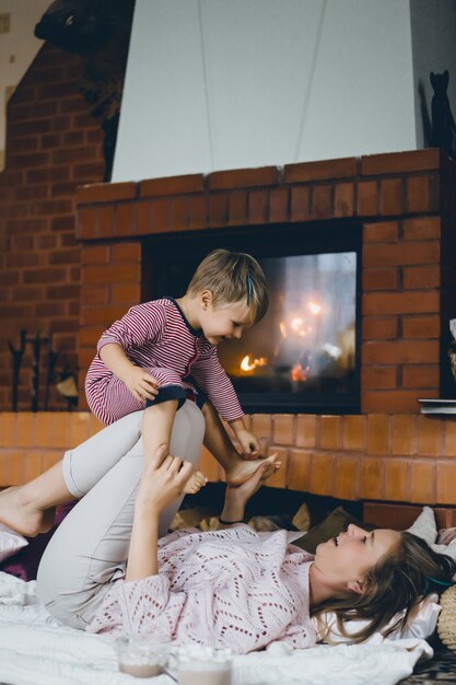 Young woman with a child. Mom and son are fooling around, having fun near the fireplace.