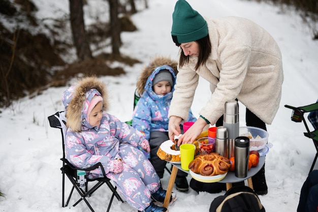Young woman with children in winter forest on a picnic Mother and three kids