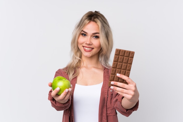 Young woman with chocolate and apple over isolated wall