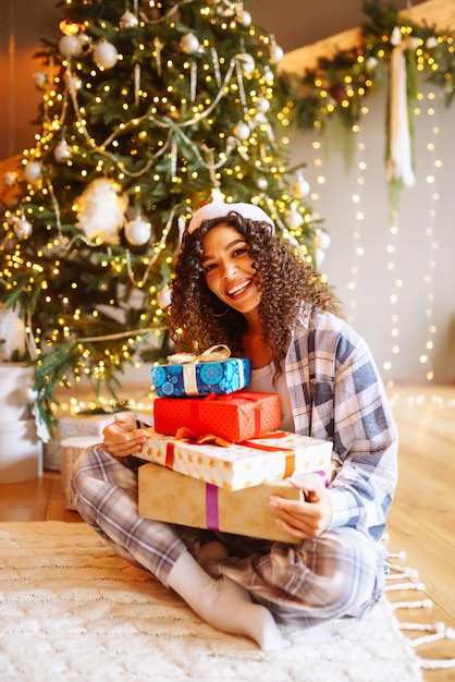 クリスマス ツリーの近くの家でクリスマス プレゼントを持つ若い女性冬の休日正月